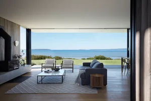 A modern living room with ocean views, featuring a sectional sofa, two armchairs, and a coffee table.