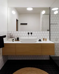 A modern minimalist bathroom with white tiles, wooden cabinets, and a wooden vanity with a white sink. The floor is covered w