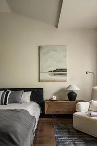 Modern, minimalist bedroom featuring a black upholstered bed and a wooden sideboard with a table lamp.