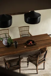 A rustic dining room featuring wooden furniture, pendant lights, and decorative elements like a plant, vase, and bowl of frui