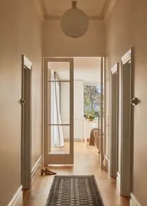 A minimalist hallway with wooden flooring and a rug, featuring a door and a light fixture.