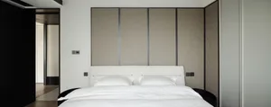 Modern minimalist bedroom with white bed, neutral-toned fabric wall panels, and black trim.