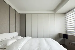 Modern minimalist bedroom with a white bed, white pillows, and a wall-mounted nightstand with a window with blinds in the bac