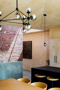 Industrial kitchen interior with brick wall, concrete counter, and wooden cabinets and stools.