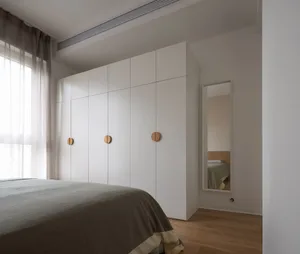 A minimalist bedroom with white walls, wooden floors, and a large window with sheer curtains.