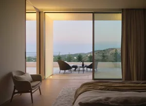 Modern bedroom with wooden flooring and glass walls overlooking scenic landscape.
