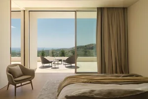 Modern bedroom featuring wooden floors, linen bedding, and glass windows with a view of the hills and sea.