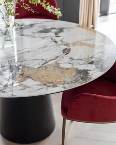 A modern dining room featuring a round marble table with a black base and red upholstered chairs.