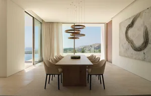 Modern dining room with a long wooden table surrounded by leather chairs, glass pendant lights hanging above, and a large win