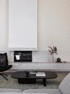 A modern living room featuring a grey marble fireplace and coffee table, with minimalist furniture and a white brick wall.