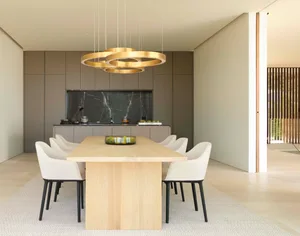 A modern kitchen-dining space with a wooden table and white chairs, featuring a gold ring chandelier and grey cabinets.