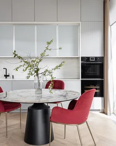 Modern residential kitchen with marble tabletop, velvet chairs, and decorative vase on the table.