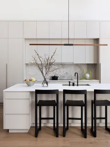 A minimalist kitchen with white cabinets, a white countertop, and black stools.