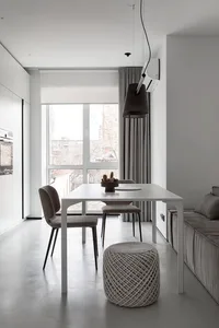 A modern minimalist living and dining room with a sleek white table and chairs, a large window, and a comfortable sofa.