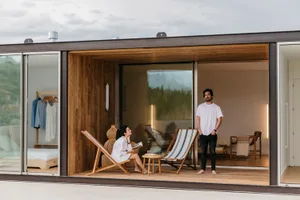 A modern living space featuring wooden flooring with a woman reading a book and a man standing and smiling.