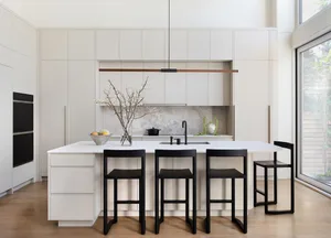 Modern minimalist kitchen with white cabinets, island, and black stools.