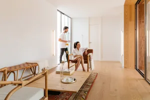 A modern minimalist living room with wooden flooring, a wooden coffee table, a leather armchair, and a white wall.