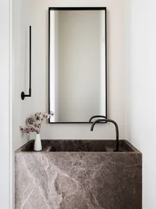 A modern minimalist bathroom featuring a marble sink, black faucet, and a vase of flowers on the counter.