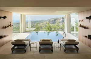 A modern relaxation room featuring a pool with a scenic mountain view, equipped with comfortable seating and tables.