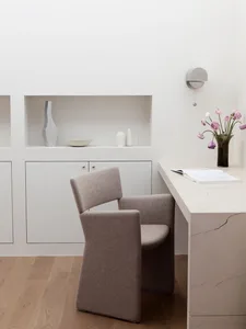 A modern study area featuring a minimalist design with a white wall, brown wooden floor, and grey chair.