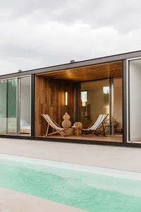 Modern vacation home with a pool and lounge area on the side featuring wooden furnishings and a light fixture.