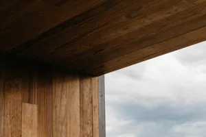 A modern window with a wooden ceiling and wall, against a cloudy sky.
