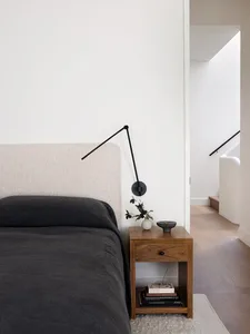 A minimalist bedroom featuring a bed with a soft, textured beige headboard, a dark grey quilt, and a wooden side table with b