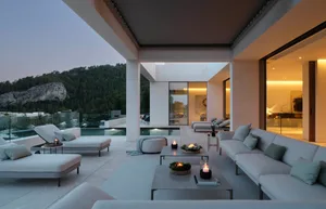 A modern outdoor living space featuring concrete flooring and furniture, with a view of mountains and trees.