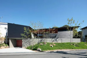 A modern residential home with a black metal-clad exterior and a green lawn in front.