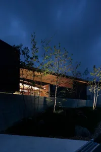 A modern minimalist house with concrete and wood exterior materials at night.