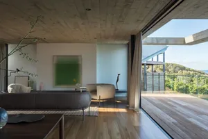 Modern minimalist living room featuring wood flooring and furniture, with large windows offering scenic views of the surround