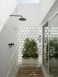 An outdoor shower with minimalist design, featuring concrete walls and a wooden platform surrounded by white rocks, with a la