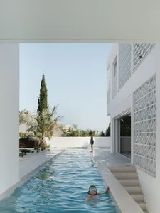 A minimalist outdoor space featuring a swimming pool with white stone and concrete finishes, surrounded by lush greenery and