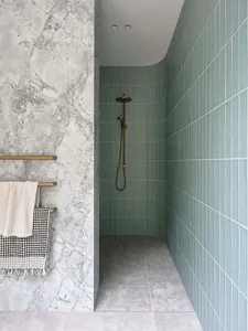 A modern bathroom with marble walls, green tiles, and a walk-in shower area.