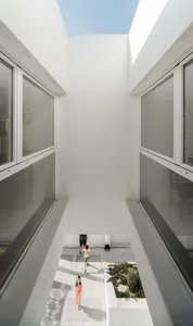 A modern house with a minimalist design featuring a central courtyard made of white concrete tiles, surrounded by clear glass