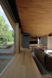 Modern living room with wooden walls and flooring, large windows overlooking greenery, contemporary furniture, and a minimali