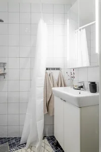 A minimalist bathroom with white tiled walls and floor, a sink, and towels hanging on hooks.