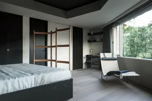 A minimalist bedroom featuring hardwood furniture and a large window with greenery outside.