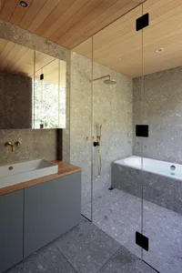 Minimalist concrete bathroom with a glass-enclosed shower, white tub, and gray cabinets.