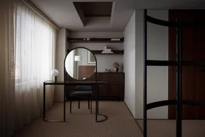 Modern minimalist interior featuring a metal-framed round mirror standing on a black desk with a small round table lamp on it