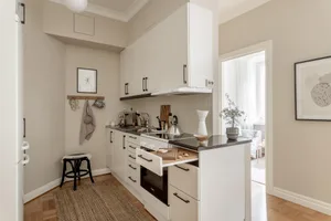 A spacious, modern, minimalist kitchen with white cabinets, a wood floor, and beige walls.
