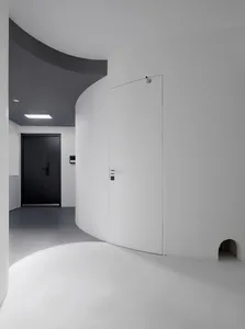 A modern entrance featuring a curved concrete wall and a black door.