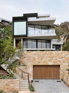 A modern house with a concrete exterior, large windows, and a stone wall.