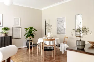 A modern interior design living room with a round wooden table, chairs, plants, and abstract art.