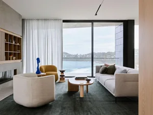 A modern living room with textured fabric furniture, large windows overlooking the ocean, and minimalist decor.