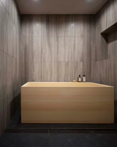 Minimalist modern bathroom with a wooden bathtub, grey stone walls, and black floor tiles.