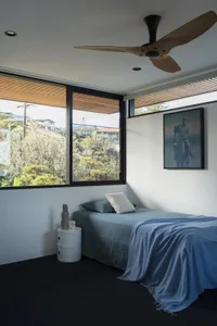 Modern minimalist bedroom featuring a blue blanket on the bed, with a white and black nightstand and large windows with bambo