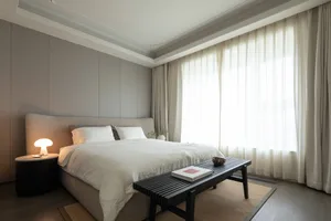A minimalist bedroom designed with gray and taupe tones, featuring a large bed with soft bedding, a side table with a table l