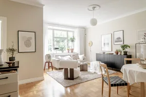 A modern, neutral-toned living room with white walls, light-colored wooden floors, and minimalistic decor.