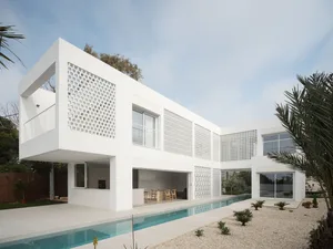 A minimalist modern house with a white concrete exterior, featuring a balcony and a swimming pool.